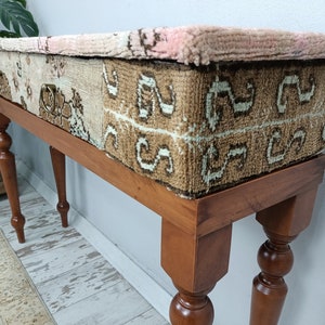 Op de afbeelding: Een houten consoletafel met een blad bekleed met een patchwork van kleurrijke tapijten. De tafel heeft vier gedraaide poten en een lade met een messing handvat.
