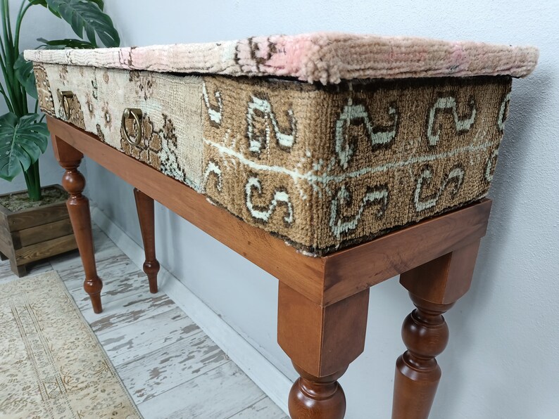 Op de afbeelding: Een houten consoletafel met een blad bekleed met een patchwork van kleurrijke tapijten. De tafel heeft vier gedraaide poten en een lade met een messing handvat.