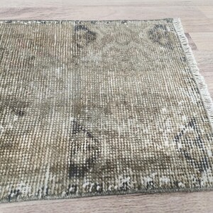 May include: A vintage-style rug with a faded, distressed look. The rug has a light brown and beige colour with a subtle pattern. The rug is made of woven fibres and has a fringed edge.