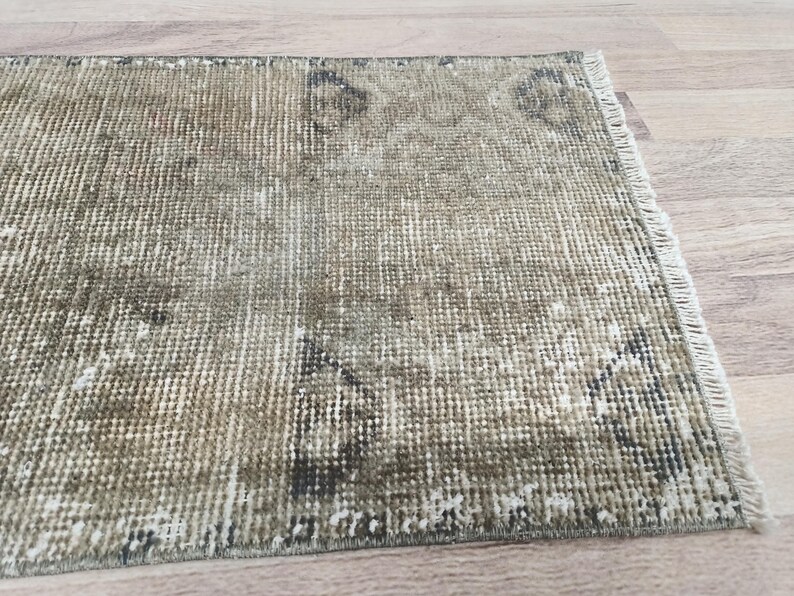 May include: A vintage-style rug with a faded, distressed look. The rug has a light brown and beige colour with a subtle pattern. The rug is made of woven fibres and has a fringed edge.