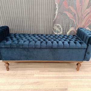 May include: A blue velvet tufted storage bench with wooden legs. The bench has a button-tufted design and a rectangular shape.