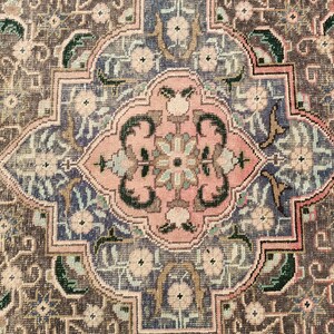 May include: A detailed close-up of a traditional rug with a central medallion design. The rug features intricate floral patterns in shades of pink, blue, green, and brown.