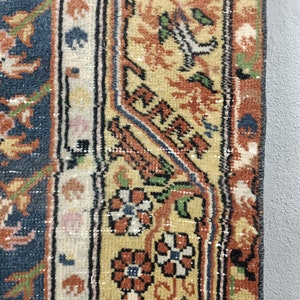 May include: Close-up of a rug with a blue background and a border of intricate floral patterns in shades of orange, yellow, and green.