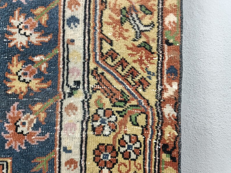 May include: Close-up of a rug with a blue background and a border of intricate floral patterns in shades of orange, yellow, and green.