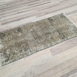 May include: A vintage-style runner rug with a faded, distressed look. The rug has a light brown background with a subtle pattern in a darker brown shade. The rug has a fringe border.