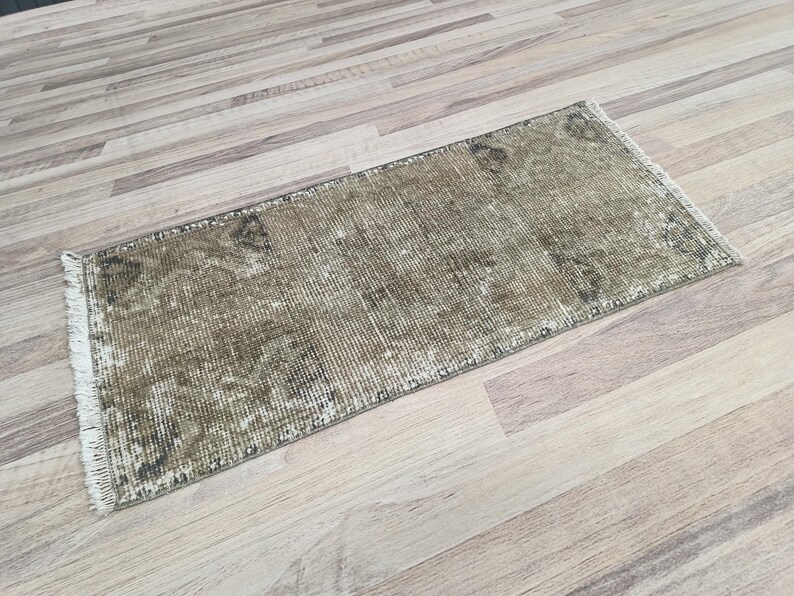 May include: A vintage-style runner rug with a faded, distressed look. The rug has a light brown background with a subtle pattern in a darker brown shade. The rug has a fringe border.