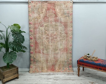 May include: A vintage rug with a faded floral pattern in shades of pink, beige, and green. The rug is hanging on a white wall.