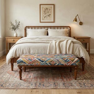 a cozy and inviting bedroom with a large bed, wooden nightstands, and a colorful patterned bench. The room has a neutral color palette with a wooden floor and a framed artwork on the wall.