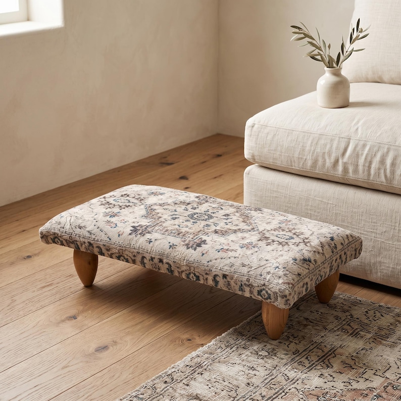 a cozy living room with a patterned ottoman, a beige sofa, and a rug on a wooden floor.