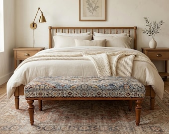 May include: A bedroom scene featuring a wooden bed frame with neutral-colored bedding, a patterned bench at the foot, and a vintage-style rug. The room is decorated with a framed botanical print and a brass wall sconce, creating a cozy and inviting atmosphere.