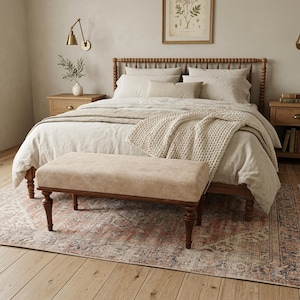 Könnte beinhalten: Ein Schlafzimmer mit einem Holzbett und Bettwäsche in neutralen Tönen, darunter eine cremefarbene Strickdecke. Am Fuß des Bettes befindet sich eine beige Bank mit Holzbeinen. Ein gemusterter Teppich und Nachttische aus Holz vervollständigen die Szene.