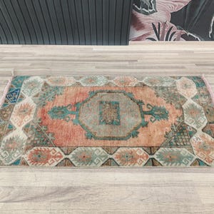 May include: A vintage rug with a faded pink, teal, and brown geometric pattern. The rug has a distressed look and is perfect for adding a touch of bohemian style to any room.