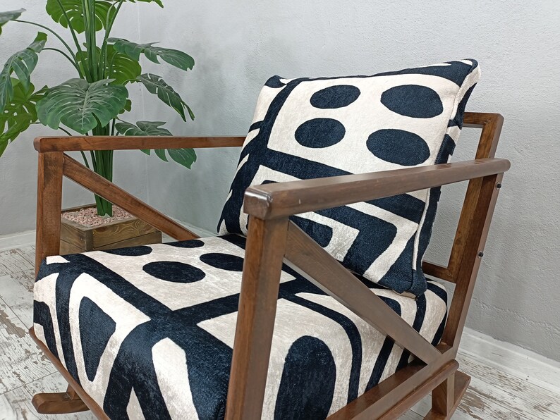 May include: A wooden rocking chair with a black and white geometric patterned cushion. The chair has a dark brown finish and a simple, classic design.
