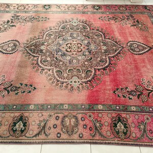 May include: A vintage Persian rug with a pink background and intricate floral patterns in shades of brown, green, and blue. The rug has a faded, distressed look, giving it a unique character.