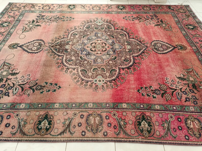 May include: A vintage Persian rug with a pink background and intricate floral patterns in shades of brown, green, and blue. The rug has a faded, distressed look, giving it a unique character.