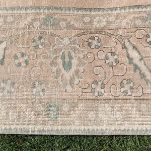 May include: Close-up of a light brown rug with a light blue and white pattern. The rug has a fringe border.