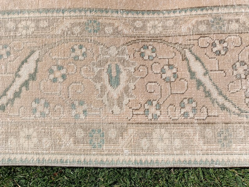 May include: Close-up of a light brown rug with a light blue and white pattern. The rug has a fringe border.