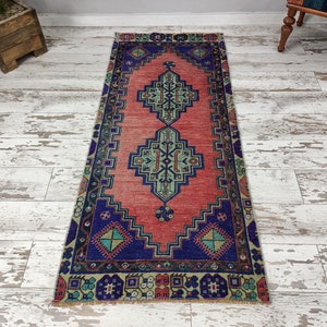 May include: A vintage runner rug with a geometric pattern in shades of red, blue, green, and beige. The rug has a distressed look and is perfect for adding a touch of bohemian style to any room.