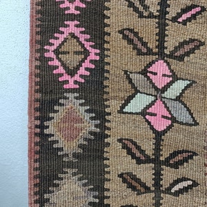 May include: Close-up of a brown and pink patterned rug with a geometric design. The rug has a fringe border and is made of woven fabric.