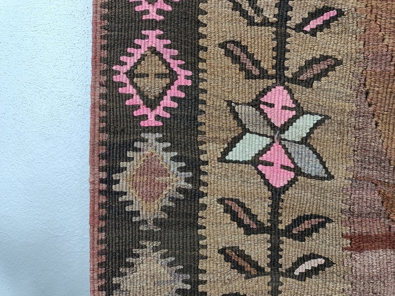 May include: Close-up of a brown and pink patterned rug with a geometric design. The rug has a fringe border and is made of woven fabric.
