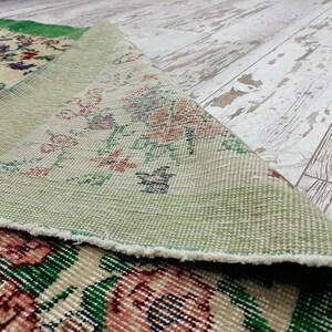 May include: Close-up of a green and cream patterned rug with a floral design. The rug is folded over, revealing the underside, which is a light green color.
