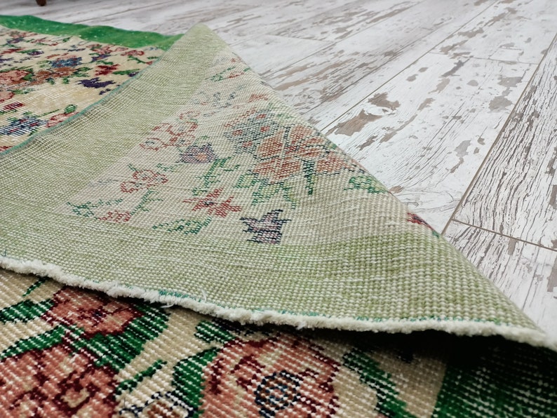 May include: Close-up of a green and cream patterned rug with a floral design. The rug is folded over, revealing the underside, which is a light green color.