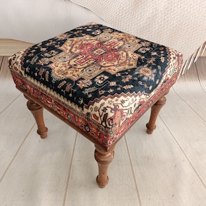 May include: A small, square ottoman with a dark blue, red and cream patterned fabric top and four wooden legs.