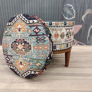 May include: A round, blue, and orange patterned ottoman with wooden legs. The ottoman has a traditional, geometric design.
