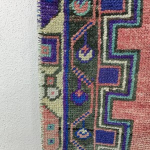 May include: Close-up of the edge of a pink, blue, and green patterned rug with a fringed edge.