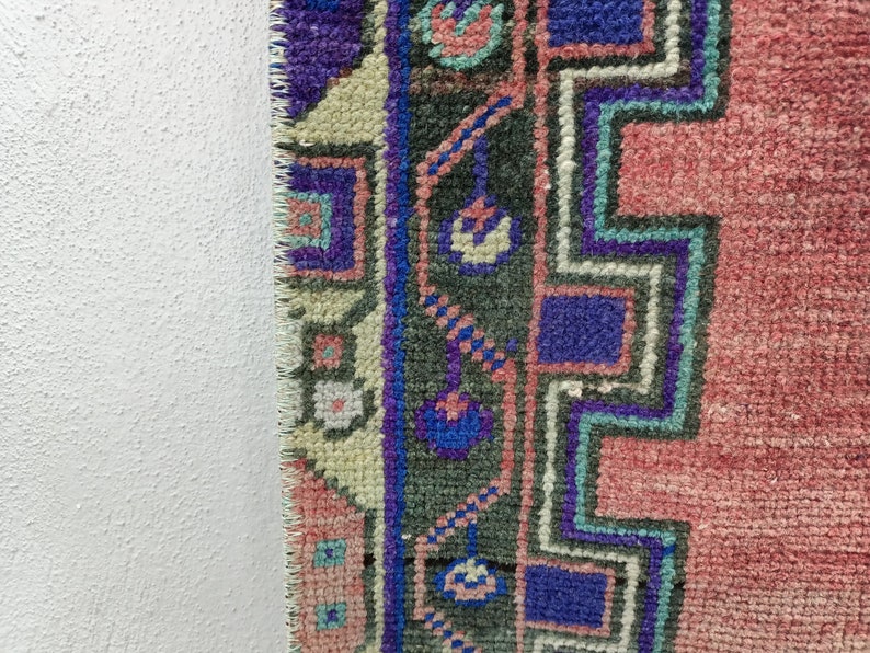 May include: Close-up of the edge of a pink, blue, and green patterned rug with a fringed edge.
