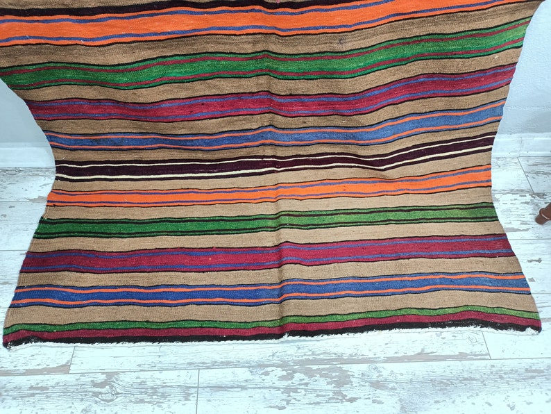 May include: A striped woven rug with a variety of colors, including brown, orange, green, blue, and red. The rug has a fringed edge and is made of natural fibers.