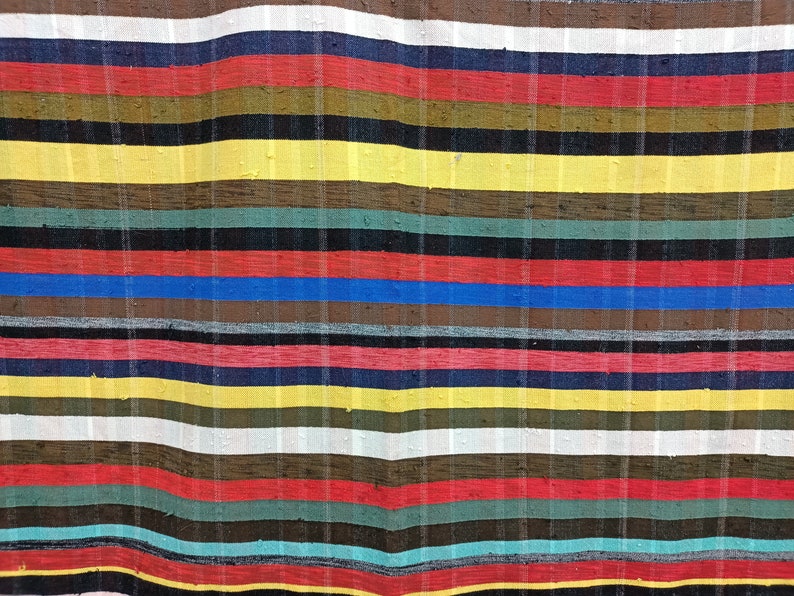 May include: A colorful striped fabric with a variety of colors, including red, yellow, blue, green, and brown. The fabric is woven with a textured pattern and has a slightly wavy appearance.