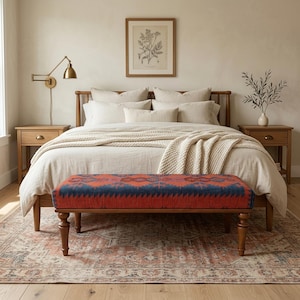 Pode incluir: Um quarto com uma cama de madeira, roupa de cama creme e um banco estampado com um design vermelho e azul. O banco está aos pés da cama. Um tapete estampado e duas mesas de cabeceira de madeira também são visíveis.