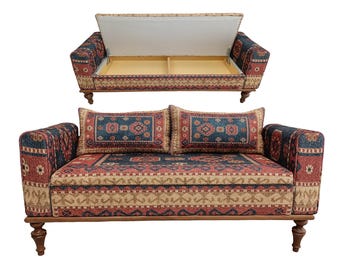 May include: A two-seater sofa with a patterned fabric in red, blue, and beige. The sofa has a wooden frame and turned legs. One sofa is shown with the seat open, revealing storage space. Two matching throw pillows are on the sofa.