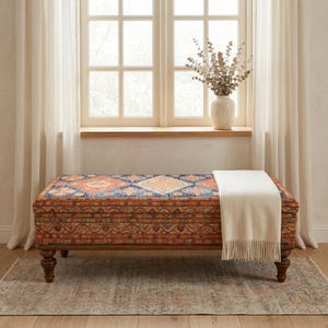 a large, colorful ottoman with a blanket draped over it, placed in front of a window with curtains.
