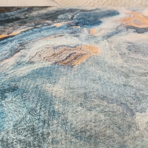 Puede incluir: Primer plano de una tela azul y blanca con un patr&oacute;n de m&aacute;rmol. La tela tiene una textura suave y peluda y est&aacute; acentuada con sutiles toques de oro.