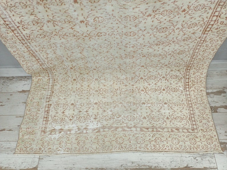 Puede incluir: Una alfombra vintage con fondo crema y un delicado patr&oacute;n intrincado en color marr&oacute;n claro. La alfombra tiene un aspecto descolorido y desgastado, lo que le da un aspecto &uacute;nico y antiguo.