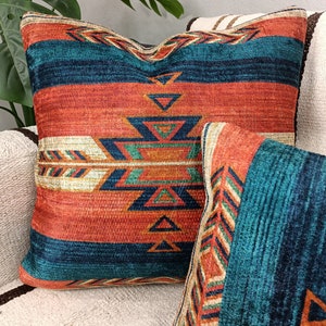 K&ouml;nnte beinhalten: Zwei dekorative Kissen mit einem s&uuml;dwestlichen Muster mit geometrischen Formen in den Farben T&uuml;rkis, Orange und Braun.