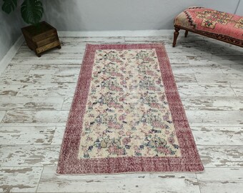 May include: A vintage floral area rug with a cream background and a pink border. The rug has a faded, distressed look and features a floral pattern in shades of pink, blue, and green.
