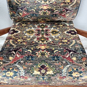 May include: A wooden armchair with a patterned fabric upholstery. The fabric features a colorful design with intricate details in shades of red, blue, green, and yellow.