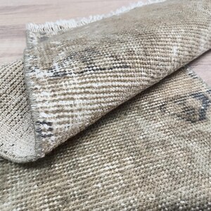 May include: A close-up of a beige and brown woven rug with a fringed edge. The rug is folded in half, showing the texture and pattern of the fabric.