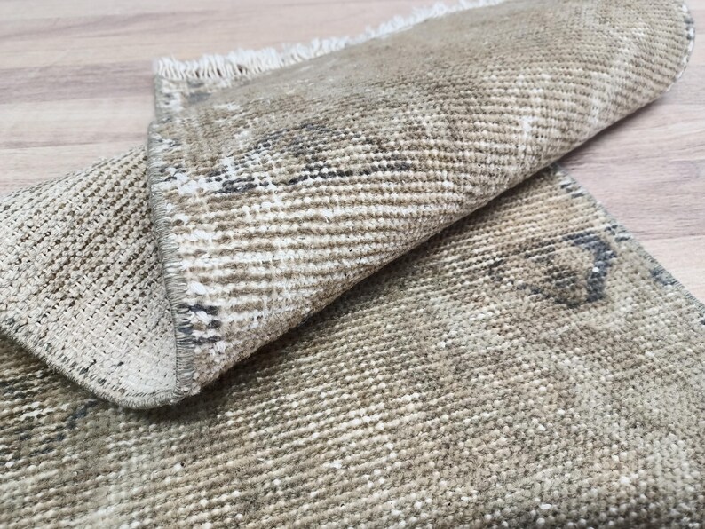 May include: A close-up of a beige and brown woven rug with a fringed edge. The rug is folded in half, showing the texture and pattern of the fabric.