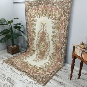 Op de afbeelding: Een vintage tapijt met een bloemenpatroon in tinten bruin, roze en cr&egrave;me. Het tapijt heeft een verweerde look en is perfect om een ​​bohemien stijl aan elke kamer toe te voegen.