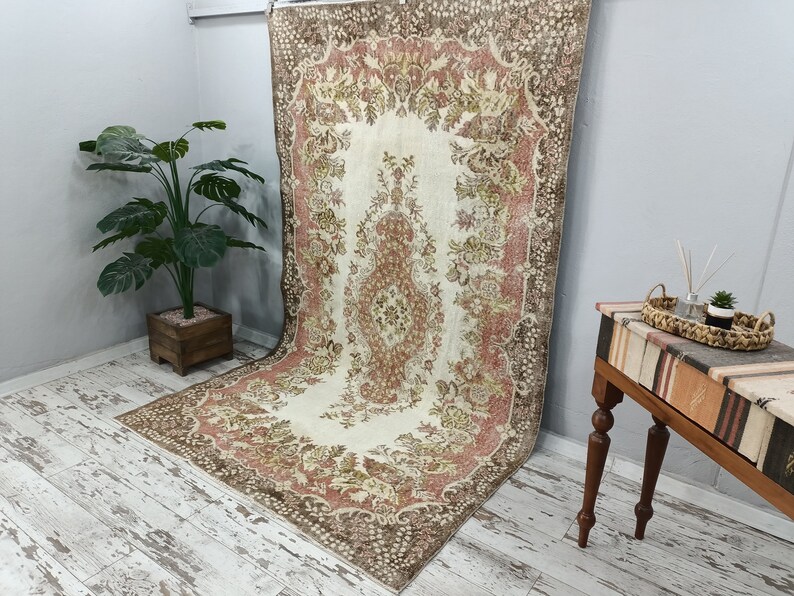 Op de afbeelding: Een vintage tapijt met een bloemenpatroon in tinten bruin, roze en cr&egrave;me. Het tapijt heeft een verweerde look en is perfect om een ​​bohemien stijl aan elke kamer toe te voegen.