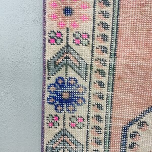 Pode incluir: Close-up da borda de um tapete rosa e creme com um padr&atilde;o floral azul e verde. O tapete tem uma borda de franjas.
