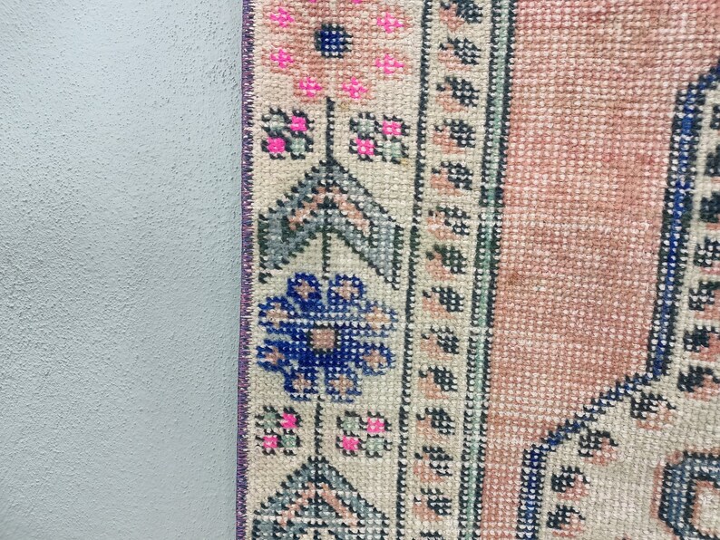 Pode incluir: Close-up da borda de um tapete rosa e creme com um padr&atilde;o floral azul e verde. O tapete tem uma borda de franjas.