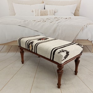May include: A white and brown patterned ottoman with wooden legs. The ottoman is sitting on a wooden floor.