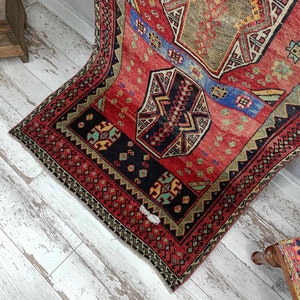 May include: A vintage Turkish rug with a red, blue, and green geometric pattern. The rug has a frayed edge and is in good condition.