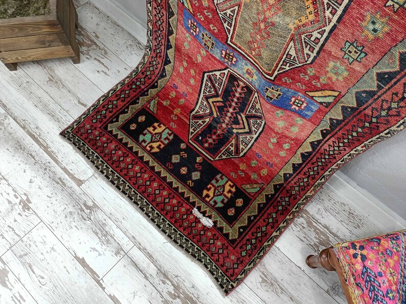 May include: A vintage Turkish rug with a red, blue, and green geometric pattern. The rug has a frayed edge and is in good condition.