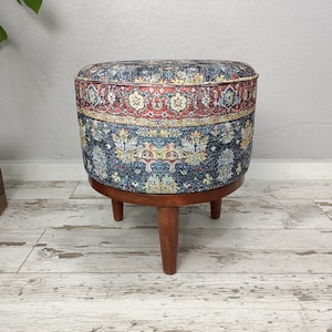 May include: A round ottoman with a blue, red, and yellow patterned fabric cover. The ottoman has a wooden base with three legs.